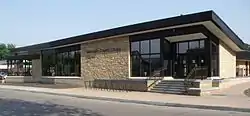 A single-story glass and limestone building from across a street on a sunny summer day