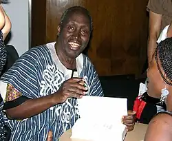 A smiling man faces the camera while opening a book