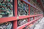 Wooden wall with red beams and colored carvings of plants, peacocks and other birds.