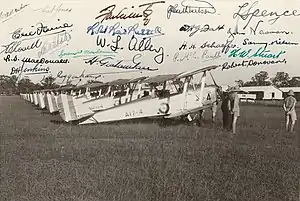 Side view of biplanes in a row at a field, along with some men in light-coloured military uniforms and pith helmets