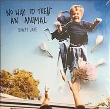 A young smiling boy is pictured thrown in the air by a set of adult hands. Flowers and petals sit atop the image, as well as a second cut-out of the boy in the same position. The sky behind the boy is bright blue and a tree is in the distance. At the top left is the album name in black capital letters along with the artist name.