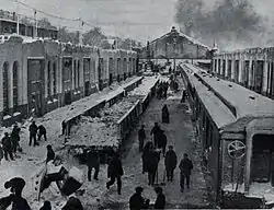 Several workers stand among trains and buildings with shovels in their hands