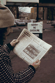 A man at a service station reads about the U.S. gasoline rationing system in an afternoon newspaper; a sign in the background states that no gasoline is available. 1974