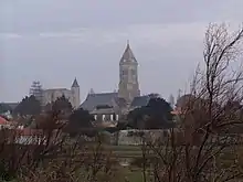 Colour photograph showing a vacant lot in the Banzeau district, with the towers of the Saint-Philbert church and the Noirmoutier castle on the horizon.