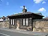 A small stone building in a single storey, with a blocked doorway and windows containing lattice tracery