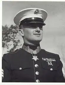 Head and shoulders of a white man with a pointed mustache, wearing a star-shaped medal on a blue ribbon around his neck.