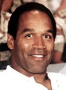 A black man smiling at a camera while wearing a white shirt.