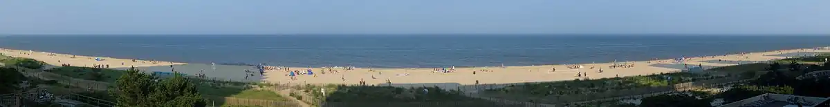 A beach with people scattered about and backlit by late afternoon sun