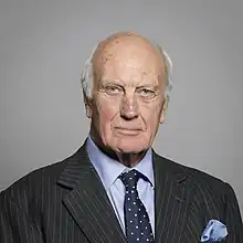 Head and shoulders of a balding grey-haired man in a pinstripe suit