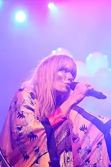 The singer is performing into a microphone while wearing a kimono and glitter is spread across her face.