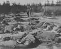 American soldiers walk past the bodies of prisoners killed during evacuation.