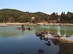 A lake with stones in the water in front of wooded hills.