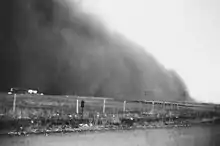 A large cloud of dust next to a farm