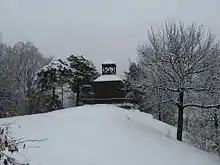 The brick building from the coin. It is seen at a distance, and snow covers the ground.