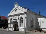 A somewhat ponderous version of the eclectic style.
Triangular pediment, horizontal and raking cornices, semi-circular cap on pediment, with rustication to windows and gable ventilator.
Porch on Ionic columns.
This impressive Edwardian building, with its neoclassical features, was erected by Matthew Deas, master-builder of Beaufort West.
The front gable bears the date 1906.
Type of site: Library
Previous use: Library.
Current use: Municipal offices.