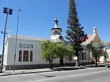 Single-story building with 5 bays. Symmetrical
roof hidden by parapet, and a bracketed cornice.
Hexagonal bell tower over clock above Donkin street entrance.
Windows with shouldered arches.
Rusticated pilasters. The Town Hall of Beaufort West stands in the main street, at the centre of the-historic Karoo town.
It is a striking building, white and massive with bold lines and an old-fashioned tower.
The origins of Beaufort West go back to 1818.
Architectural style: Eclectic.
Type of site: Town Hall
Previous use: Town Hall.
Current use: Museum.

This building is the first Town Hall of the first Municipality in the country and was built in 1865-1866 by James Bisset.
It accommodated the town council, public library, post office, and police station.
it is now part of Beaufort West Museum, it houses a display of Prof Chris Barnard, the first doctor to perform a heart transplant.