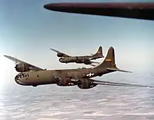 Two large olive-colored aircraft flying over farmland.