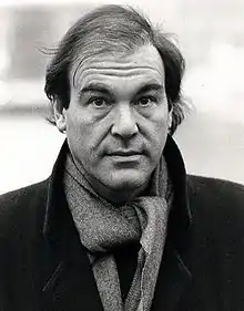 A man, wearing a coat and scarf, furrows his brow.