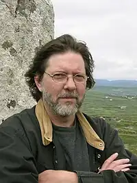 Head and shoulders photo of a man in a jacket with a beard and moustache looking into the camera.