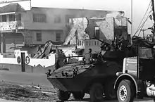 photograph of a Marine LAV-25 and utility truck in the foreground with a partially destroyed building in the background