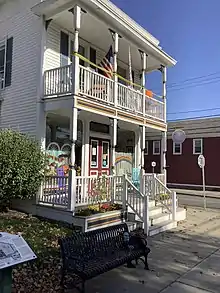 A two-story building with a porch on the first floor, and a balcony with a matching railing on the  2nd floor.