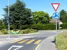 A roundabout with a pedestrian crossing across one arm, except the crossing stripes are yellow.