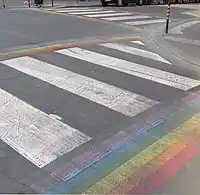 Zebra crossing with rainbow stripes running perpendiculary along its sides.