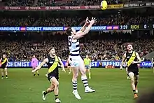 Male athlete in mid-air with arms extended overhead in readiness to mark a football