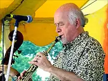 A man wearing a patterned dress shirt, performing a wind instrument while standing behind a microphone