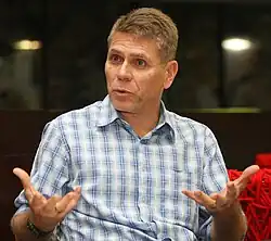 Paulo Autuori is leading a discussion. He is an older man wearing a buttoned-up shirt with sky blue figures on a white background.