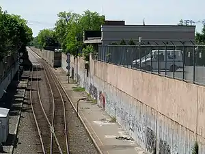 Disused platforms next to an active railway line in a cut, with a one-story midcentury building at right