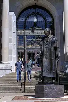 Two students walk out of Pogue Library near the statue of founder Rainey T. Wells.