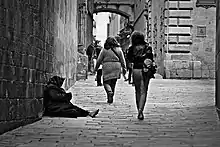 A woman sitting on the street with two woman walking past her.