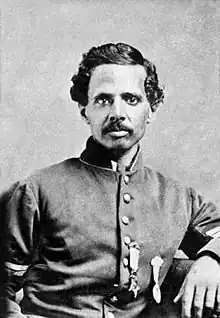 Head and shoulders of a black man with wavy hair and mustache wearing a jacket with stripes on the upper sleeves and two medals hanging from ribbons on his left breast. He left arm is propped on an object to his side.