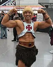 Man dressed as He-Man is looking at the camera and smiling. He has taken a pose, showing off his biceps.