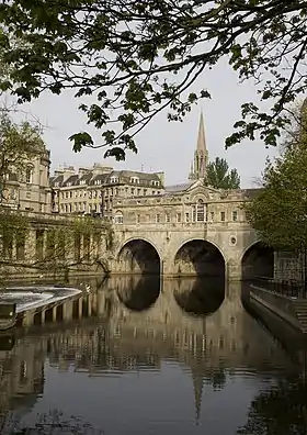 Water in the foreground reflecting an arched bridge of honey coloured stone.