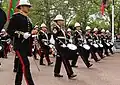 A band during the  funeral procession of Elizabeth II (flanked by a Director of Music as a marker). The side, tenor and bass drums are wrapped in black cloth during a funeral procession.