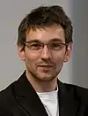 A man with short hair in a black coat wearing glasses.