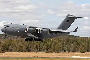 Colour photo of a grey military aircraft flying just above the ground with its wheels extended