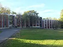 Pictured: Rothschild, Garrison, and Taylor Residence Halls (left to right) housed in one continuous, multi-level building. There are two visible entrances. The entrance connecting Rothschild and Garrison is one floor above the entrance connecting Garrison to Taylor, as the path along the building is at a slight incline. There are large rock formations visible in front of the building between the entrances, and medium-sized trees on the small patch of grass in front of the building.