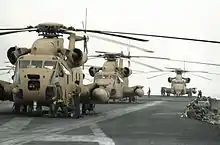 three sand painted RH-53 Sea Stallion helicopters sit on the flight deck of an aircraft carrier