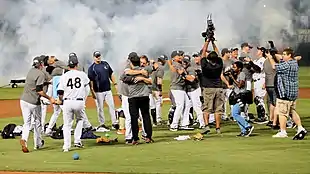 Men in white baseball uniforms with navy pinstripes hugging and celebrating on a baseball field