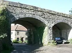 Two arches of a stone and brick bridge with a car beneath.