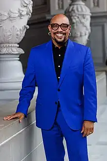 Image of Ralph Remington, standing at San Francisco City Hall, wearing a blue suit and glasses.