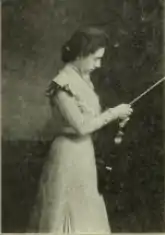 A white woman standing, holding a violin and bow