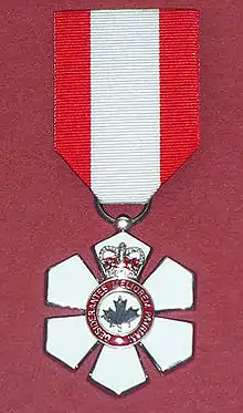 Six-pointed medallion adorned by the coat of arms of Canada, suspended from a red and white ribbon