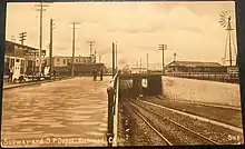 A postcard of a road and streetcar line passing under a rail line in an urban area