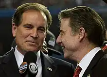 Jim Nantz holding microphone next to Rick Pitino