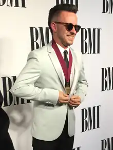 Ricky Reed in a grey suite and black tie with sunglasses on