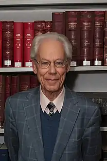 Heine stands in front of a bookshelf.